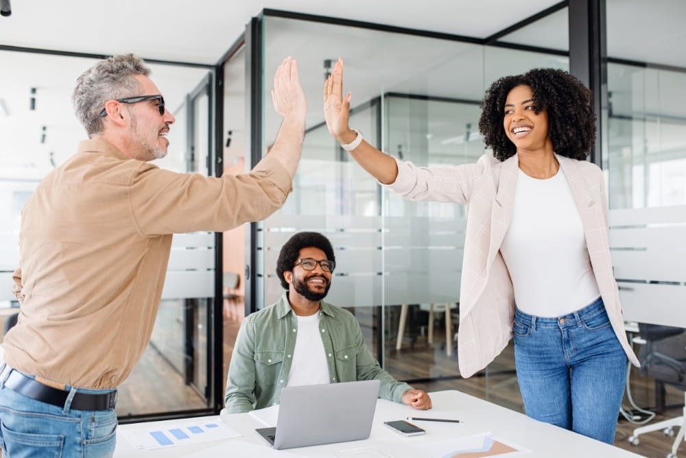 Team celebrating success with high five as a form of workplace recognition and appreciation