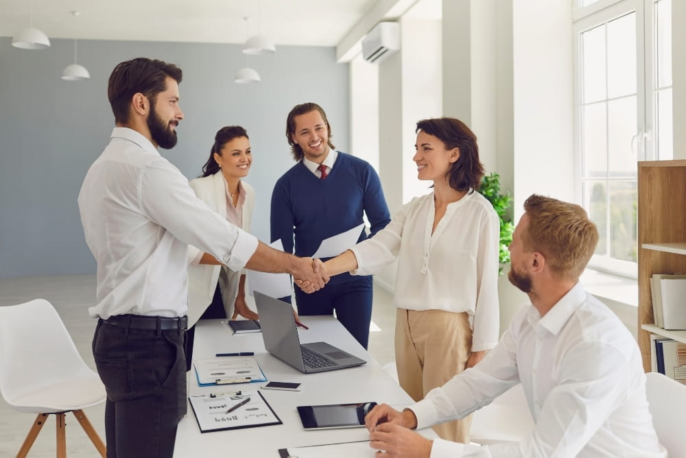 Business professionals shaking hands during a team meeting, representing modern HR leadership, employee engagement, and systemized people operations for hybrid and remote-ready organizations.
