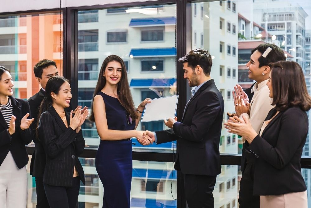 Sales employee receiving an achievement award as colleagues applaud